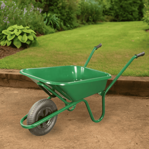 Green Walsall HD wheelbarrow with a 90L pressed steel pan and pneumatic tyre, placed on a compacted soil surface in a landscaped garden with lush grass and dense green foliage in the background