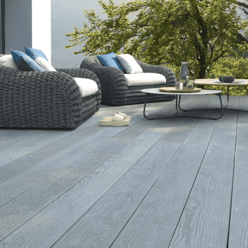 Modern garden patio featuring stylish grey Millboard Enhanced Grain composite decking boards with a realistic wood grain texture, paired with contemporary rattan outdoor furniture and a scenic garden backdrop